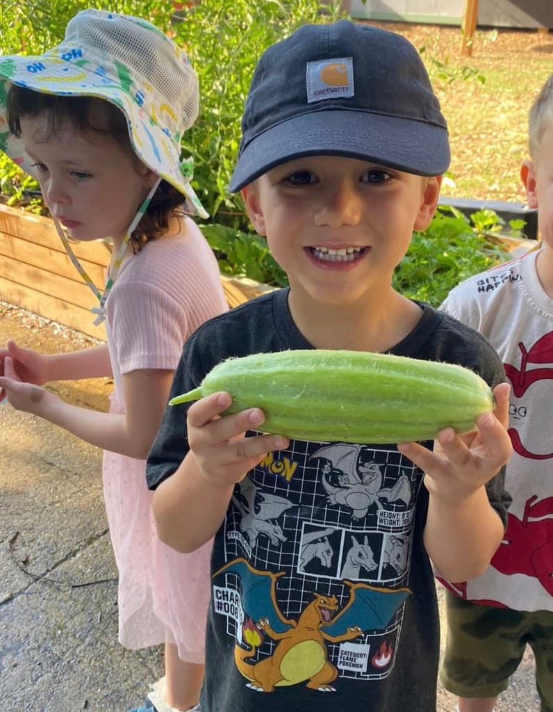 A student proudly holding a freshly harvested cucumber from the garden